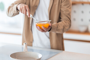 Close-up of a man's hands, holding a bowl with beaten eggs and making an omelet.