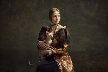  Portrait of pretty young girl in elegant retro clothing over dark vintage background posing with sphynx cat. Lady with ermine remake. Concept of history, renaissance art remake, comparison of eras