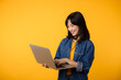 © Jirawatfoto - portrait young happy woman wearing yellow t-shirt and denim shirt holding laptop and use notebook isolated on yellow studio background. business technology application communication concept.