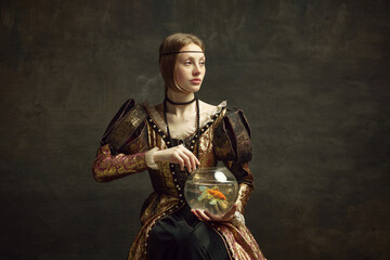 portrait of royal person, young girl in vintage dress holding large aquarium against dark green back