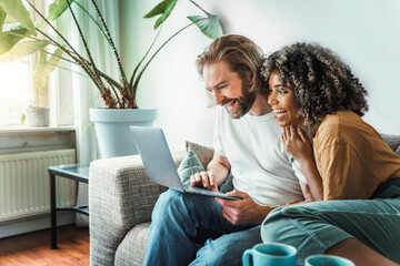multiracial young couple watching computer laptop sitting on the sofa at home - happy diverse husban