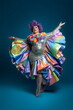 full length portrait of a happy curvy drag queen with rainbow ruffle dress isolated on blue, made with generative ai	