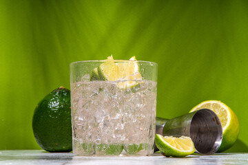 Cold iced Ti punch alcohol cocktail, small punch, rum-based mixed drink with fresh lime slice garnish, on high-colored green background