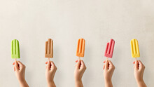 Hands holding different types of colorful fruit popsicles