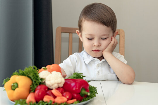 Wall Mural - kid doesn't like healthy food concept, sad, unhappy boy next to a dish of fresh vegetables