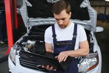 With laptop. Adult man in uniform works in the automobile salon.