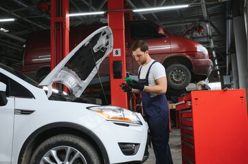 With tool in hand. Adult man in colored uniform works in the automobile salon