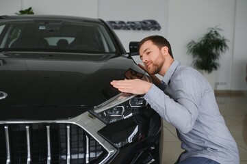 Wall Mural - Visiting car dealership. Handsome bearded man is stroking his new car and smiling