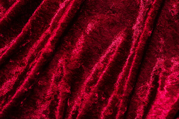 Texture of red velor corduroy fabric with folds.