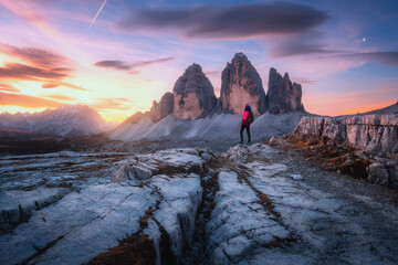 Wall Mural - Woman on the mountain trail and high rocks at colorful sunset in autumn. Tre Cime, Dolomites, Italy. Beautiful landscape with girl on path, cliffs, purple sky with pink clouds in fall. Hiking. Travel