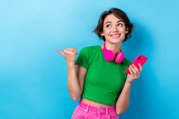 Poster - Photo of dreamy funky woman wear green t-shirt listening songs modern device pointing thumb empty space isolated blue color background