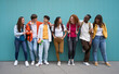 Multiracial group of cheerful erasmus students enjoying free time. Young friends together leaning against a blue wall and looking at each other smiling. Generation z and youth relationships.