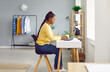 © Studio Romantic - Happy young African American woman sitting at desk in cozy home interior, using laptop computer, working on business project or studying new information on the internet. Side, profile view