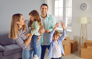 Happy family with two children are happy to move to new apartment. Young loving parents with their children have fun together in the living room of new house. Moving, buying or renting home.