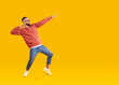 Cheerful man having fun showing dance moves in dab style on orange background in studio. Caucasian man in youth casual clothes jokingly fools around near copy space. Fun concept. Full length.