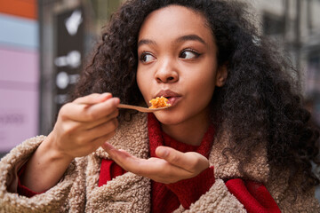 Smiling lady is eating asian food with fork and looking away while relaxing