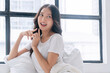 © kaew6566 - Lovely asian woman casual attire sitting with pillow beside windows relax peaceful in morning at home. Cheerful healthy young girl resting on white pillow with sunlight looking something in bed room.