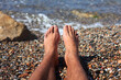 Man Feet Relax on The beach Pebbles. Relaxation and summertime concept. The young male setting showing his Legs against the sea 