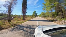 CLOSE UP: White Car Driving On Asphalt Road Through Beautiful Adriatic Landscape. Winding Paved Roadway Carved Into Rough Rocky Landscape And Surrounded With Lush And Diverse Mediterranean Growth.