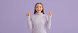 Happy young woman pointing at something on lilac background