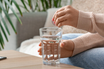 Woman putting effervescent tablet into glass of water