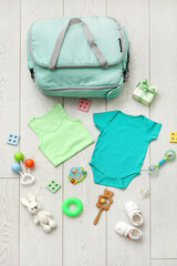 Wall Mural - Stylish bag with clothes and toys for baby on light wooden background