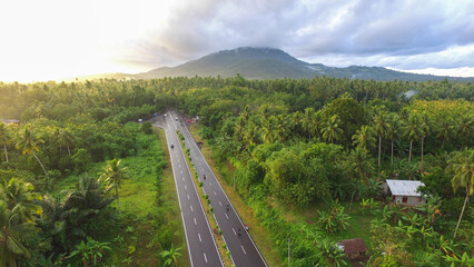 Aerial photo of the highway dividing the forest and villages with a mountain background.