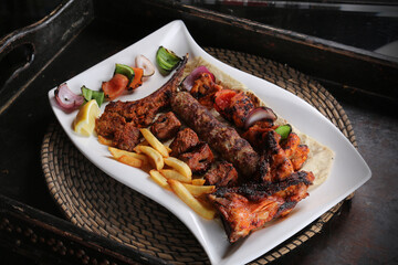 Wall Mural - Mix grill with lamb chop, chicken tikka, shish tawook, beef kabab, fries and salad served in dish isolated on red mat top view on table arabic food