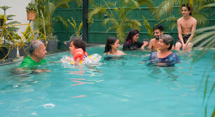 Happy Indian group family in swimming pool enjoy summer vacation picnic cheerful teen girl friend boys fun in blue water park with active senior parents cute child relax floating ring tube at resort