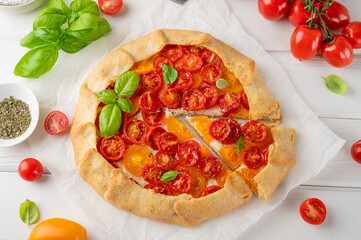 Wall Mural - Tomatoes galette or pie with cheese and herbs on a white wooden background. Vegetarian dish. Selective focus.