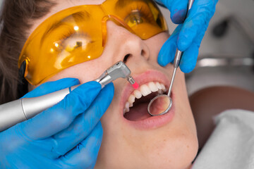 Female dentist removes tartar from her teeth.Visit is carried out in a professional dental clinic. Woman is sitting on a dental chair. Drilling and treatment of the tooth, filling.