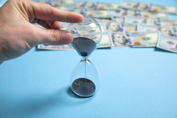 Wall Mural - Male hand holding hourglass over dollars. Time is money