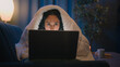 © Yuliia - Hispanic freelancer girl Latino woman Indian Arabian female at night evening home at couch sofa under blanket cover duvet working with laptop watching movie at computer browsing social media addict