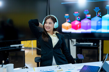 Asia business woman relaxing and listening music on the headphones while enjoying a break to stretch with hands behind her head in an office alone at work.