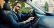 © serg - Handsome bearded 25-30-aged modern guy man sitting in front of the handlebar of his own lux class auto and applying navigator.