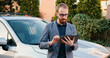 © serg - Attractive and smart adult business man holding in hands tablet, standing near car in parking lot in residential area . Outdoors. Busy lifestyle