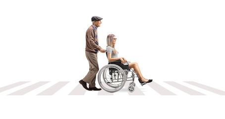 Wall Mural - Full length profile shot of an elderly man pushing a young woman in a wheelchair at a pedestrian crossing