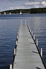 Wall Mural - footbridge reaches into a lake with sailing boats in the background