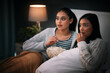 Popcorn, eating and people or friends with horror movies, scary show and sleepover on bed, streaming service or television. Gen z women relax in bedroom for drama TV film, home cinema or subscription
