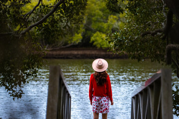 Wall Mural - Beautiful girl wearing a hat stands on boardwalk and looks at  Maroochy River and mangroves in sunshine coast region, queensland, australia; Maroochy Wetland Sanctuary