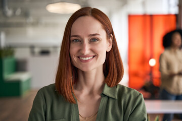 Wall Mural - Closeup portrait of confident smiling red haired businesswoman, successful CEO looking at camera in modern office. Happy student standing in university campus, education