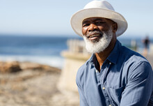 Portrait Of Happy Senior African American Man With Sun Hat On Promenade At Seaside