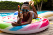 © Wavebreak Media - Portrait of happy african american girl in sunglasses lying on inflatable by pool holding ice cream