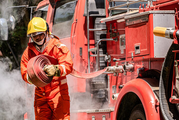 Wall Mural - Firefighter's trained muscles moved with precision effortlessly lifting and maneuvering the water hose into position ready to unleash a powerful stream of water to combat the fire's fury.