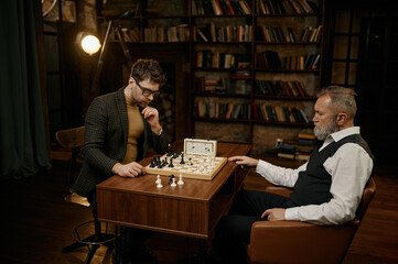 Concentrated chess players holding competition match at home library room