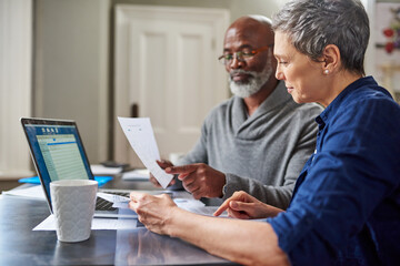 Laptop, documents and finance with a senior couple busy on a budget review in the home together. Accounting, taxes or investment planning with a mature man and woman looking at insurance or savings