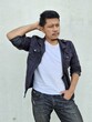 © Igunt - Cool modern young hipster man with a stylish hairstyle in a white T-shirt puts on a vintage black denim jacket. Attractive urban guy posing near a white wall. Fashionable spring menswear.