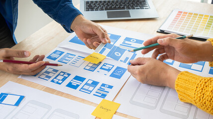 Close-up ux developers and ui designers use augmented reality to brainstorm on mobile app interface wireframe designs on modern office desks. Creative digital development office