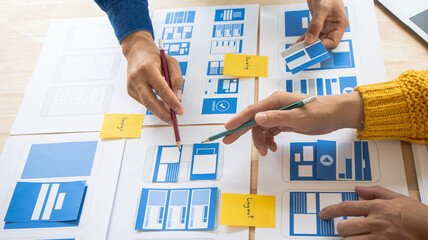 Close-up ux developers and ui designers use augmented reality to brainstorm on mobile app interface wireframe designs on modern office desks. Creative digital development office