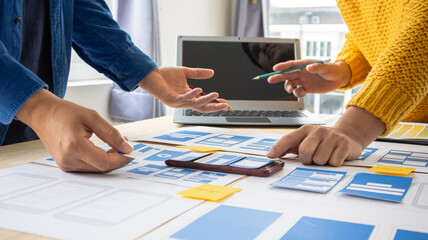 Close-up ux developers and ui designers use augmented reality to brainstorm on mobile app interface wireframe designs on modern office desks. Creative digital development office